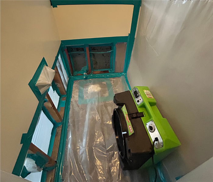 An air scrubber is operating inside a sealed containment area, set up as part of mold remediation preparations by SERVPRO Tea